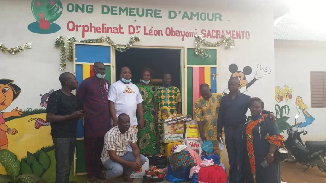 Un groupe de personnes posant devant un bâtiment orphelinat avec des paquets de dons devant l'entrée décorée d'illustrations colorées