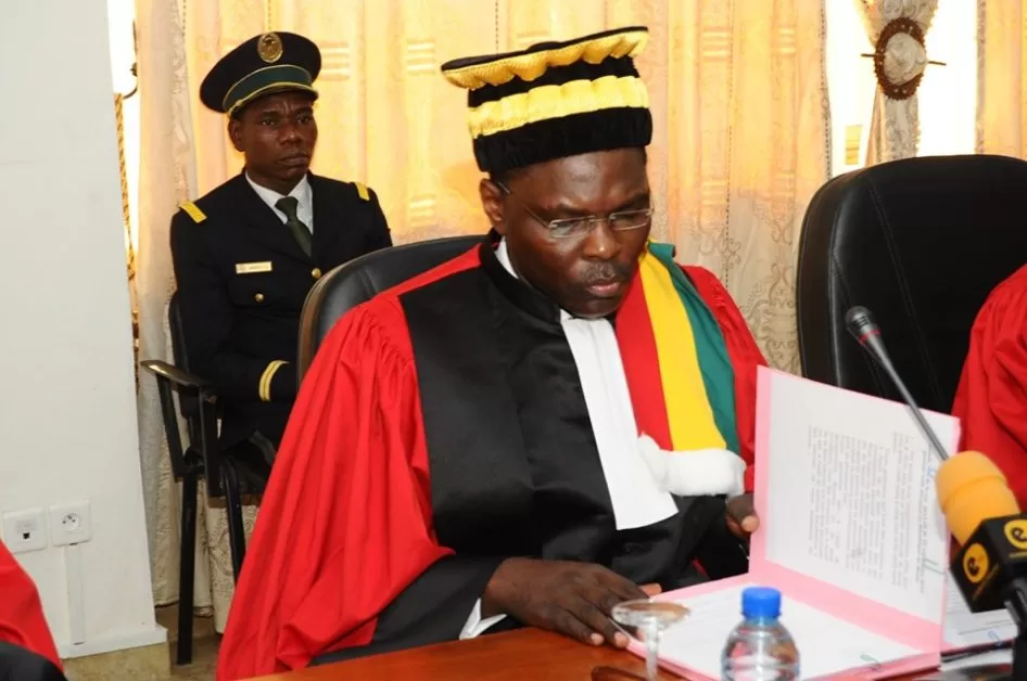 Homme en tenue judiciaire rouge et noire consulte un document ouvert lors d’une réunion officielle en intérieur