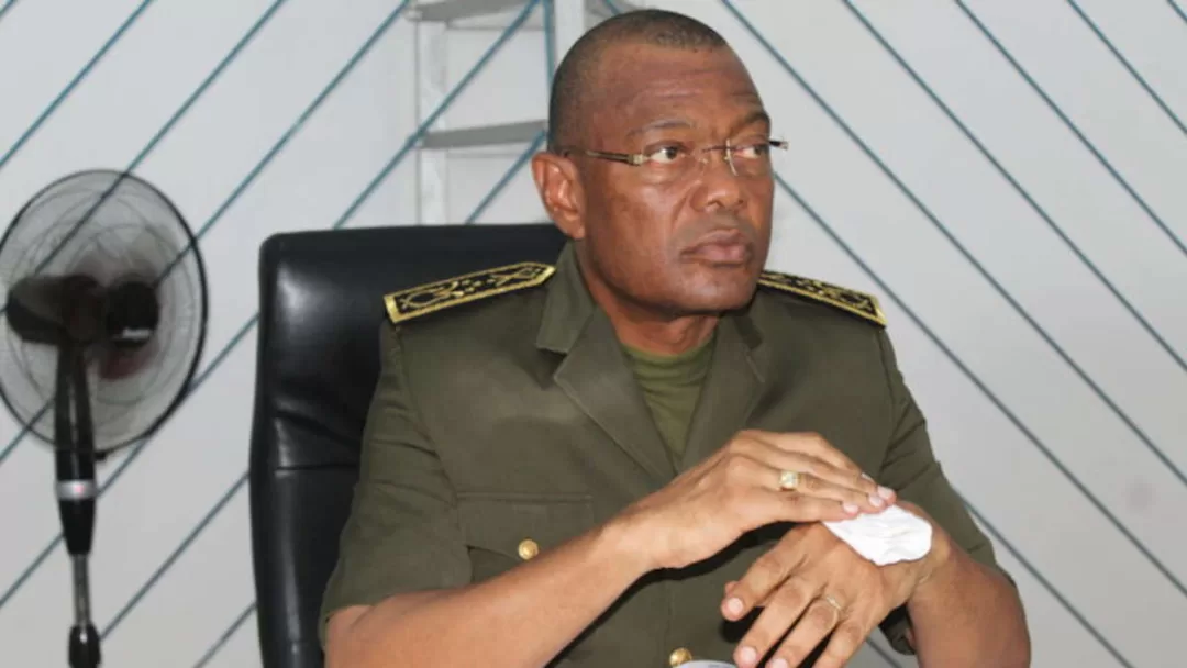 Un homme en uniforme militaire assis, regardant à droite, essuie sa main avec un mouchoir blanc