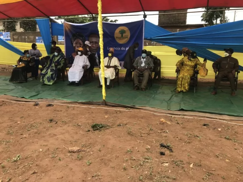 Groupe de personnes assises sous une tente avec une banderole bleue affichant un logo et du texte partiellement lisible