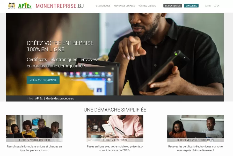 Un homme montre quelque chose sur une tablette à une personne assise devant un ordinateur portable avec écran coloré.