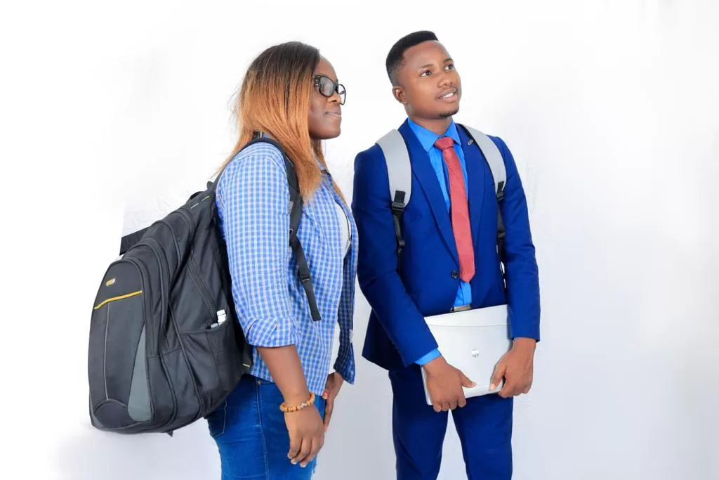 Deux étudiants debout avec sacs à dos, l’un en chemise à carreaux et l’autre en costume bleu avec cravate rouge, regardant à droite