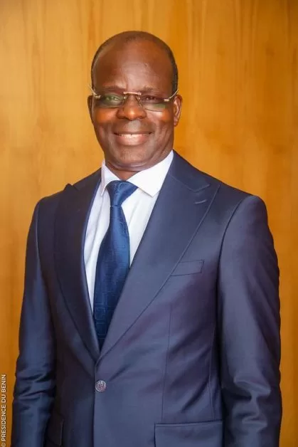 Homme souriant en costume bleu et cravate posant devant un fond en bois clair