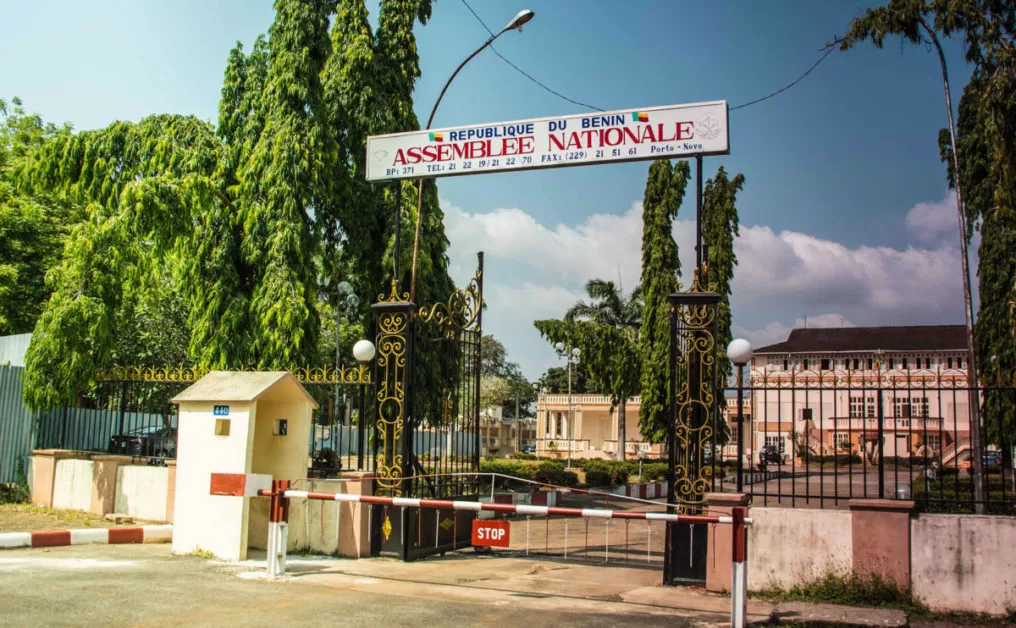 Entrée principale d un bâtiment avec un portail noir orné et une enseigne « Assemblée Nationale » sous un ciel bleu partiellement nuageux