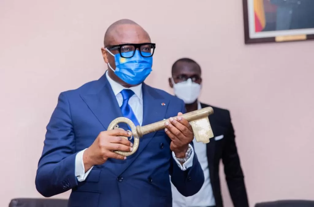 Un homme en costume bleu et masque tient une grande clé dorée avec une autre personne masquée en arrière-plan
