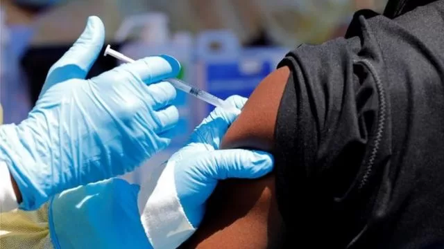 Un professionnel de santé en gants injecte un vaccin dans le bras d’une personne habillée en noir