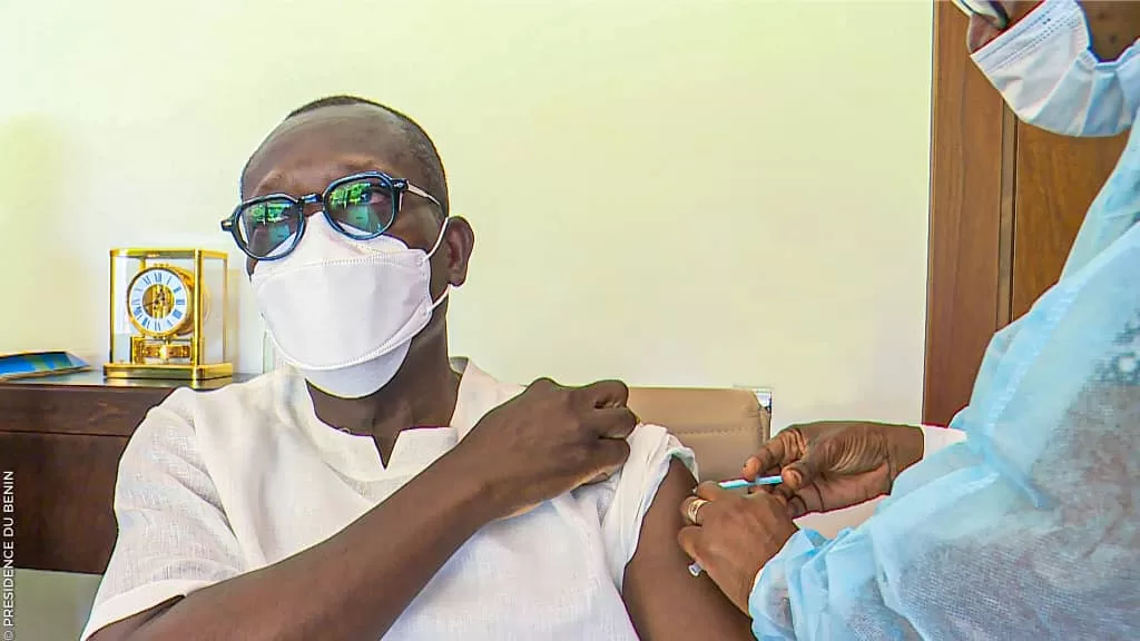 Un homme en lunettes et masque reçoit une injection dans le bras par un professionnel en tenue médicale bleue