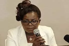 Femme en tailleur blanc parlant au micro lors d une réunion assise devant un mur beige