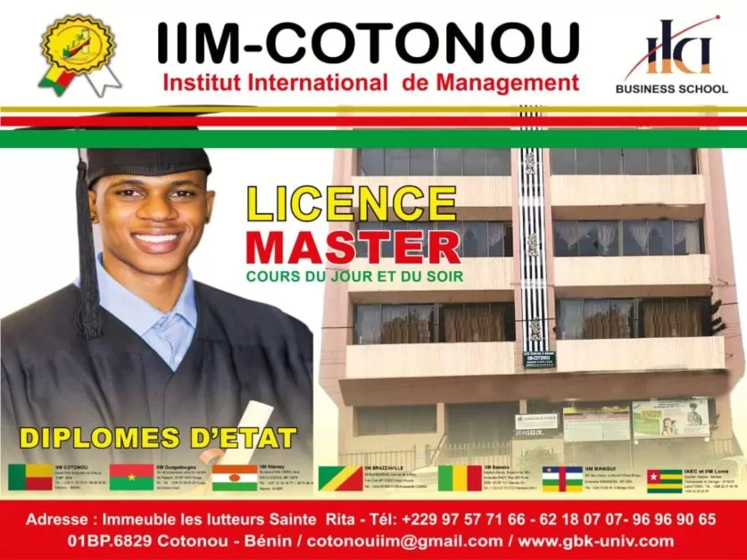 Jeune diplômé en toge et à la coiffe souriant à côté d’un bâtiment abritant une école de management international