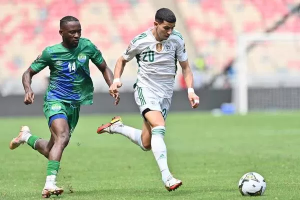 Deux joueurs de football courent à vive allure vers le ballon sur un terrain en gazon vert