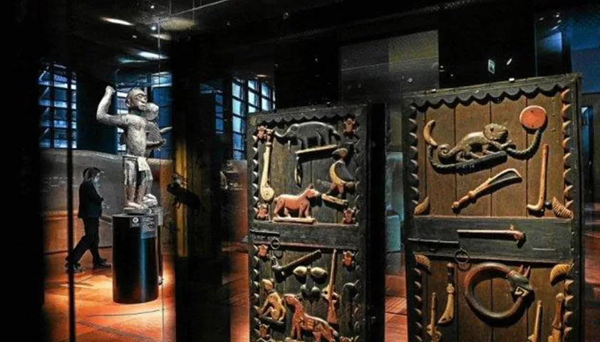 Salle d’exposition obscure avec sculptures et panneaux sculptés éclairés au mur et sur socle