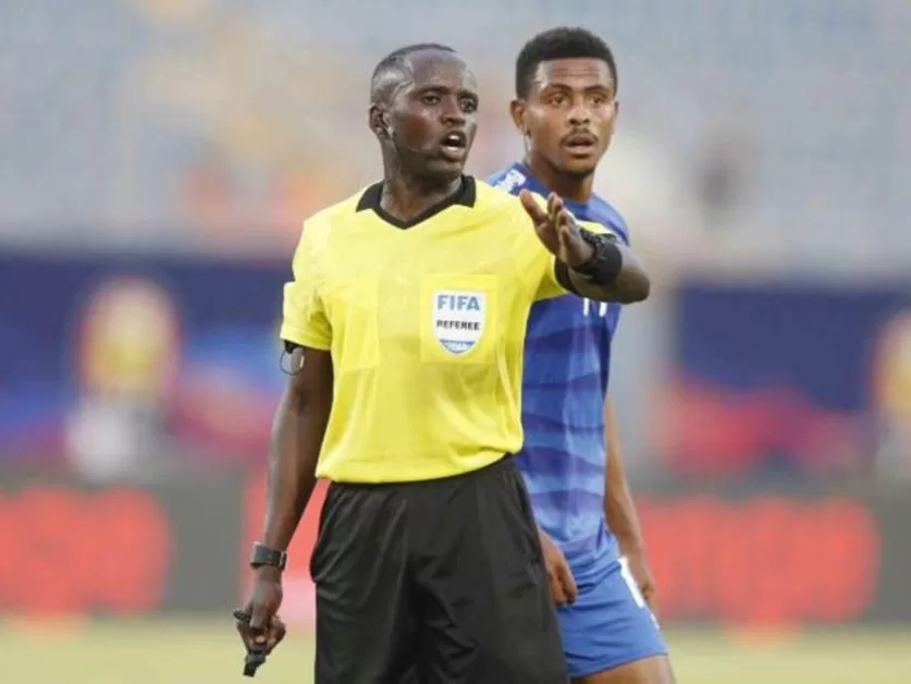 Un arbitre en maillot jaune donne des instructions à un joueur en tenue bleue lors d’un match de football