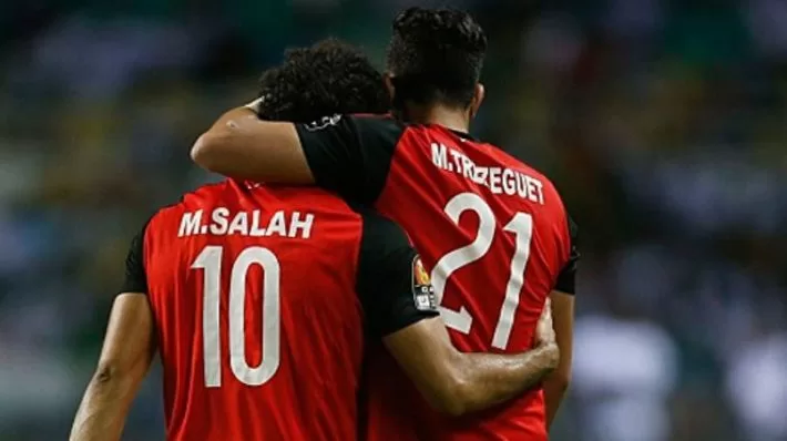 Deux joueurs de football en maillot rouge avec noms et numéros vus de dos s'enlacent sur le terrain
