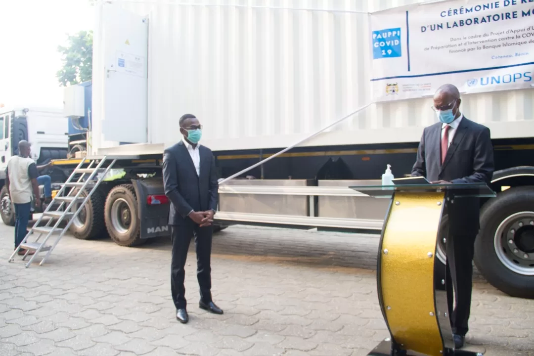 Deux hommes en costume et masque se tiennent devant un laboratoire mobile installé sur un camion blanc