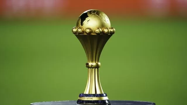 Trophée doré posé sur un socle noir avec un fond flou de terrain vert et rouge
