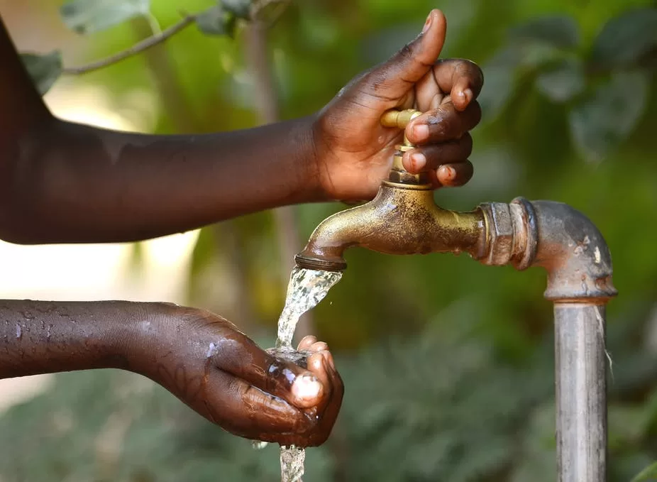 Mains noires recueillant de l'eau claire qui coule d'un robinet en extérieur avec un arrière-plan flou de verdure