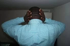 Un homme de dos se tient la tête avec les mains dans une pièce sombre