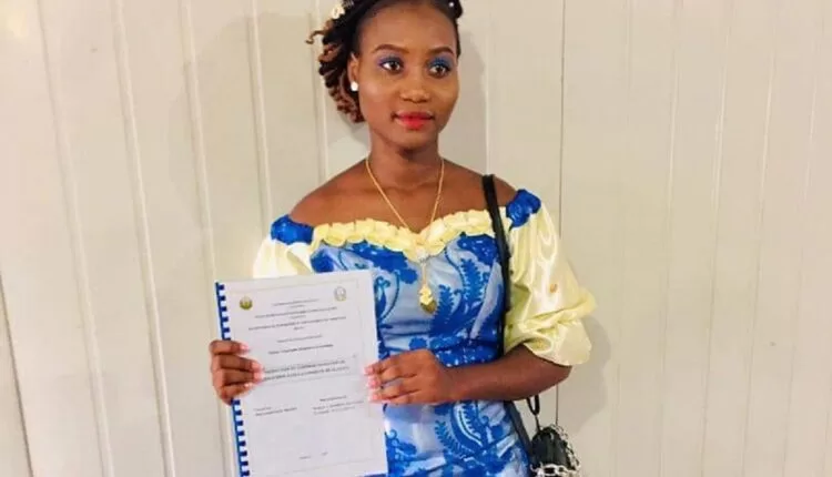 Jeune femme en robe traditionnelle bleue et jaune tenant un document relié devant un mur clair