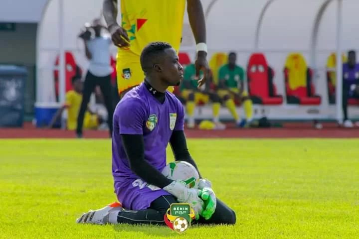 Un gardien de but en tenue violette est à genoux sur le terrain de football en tenant le ballon pendant un match