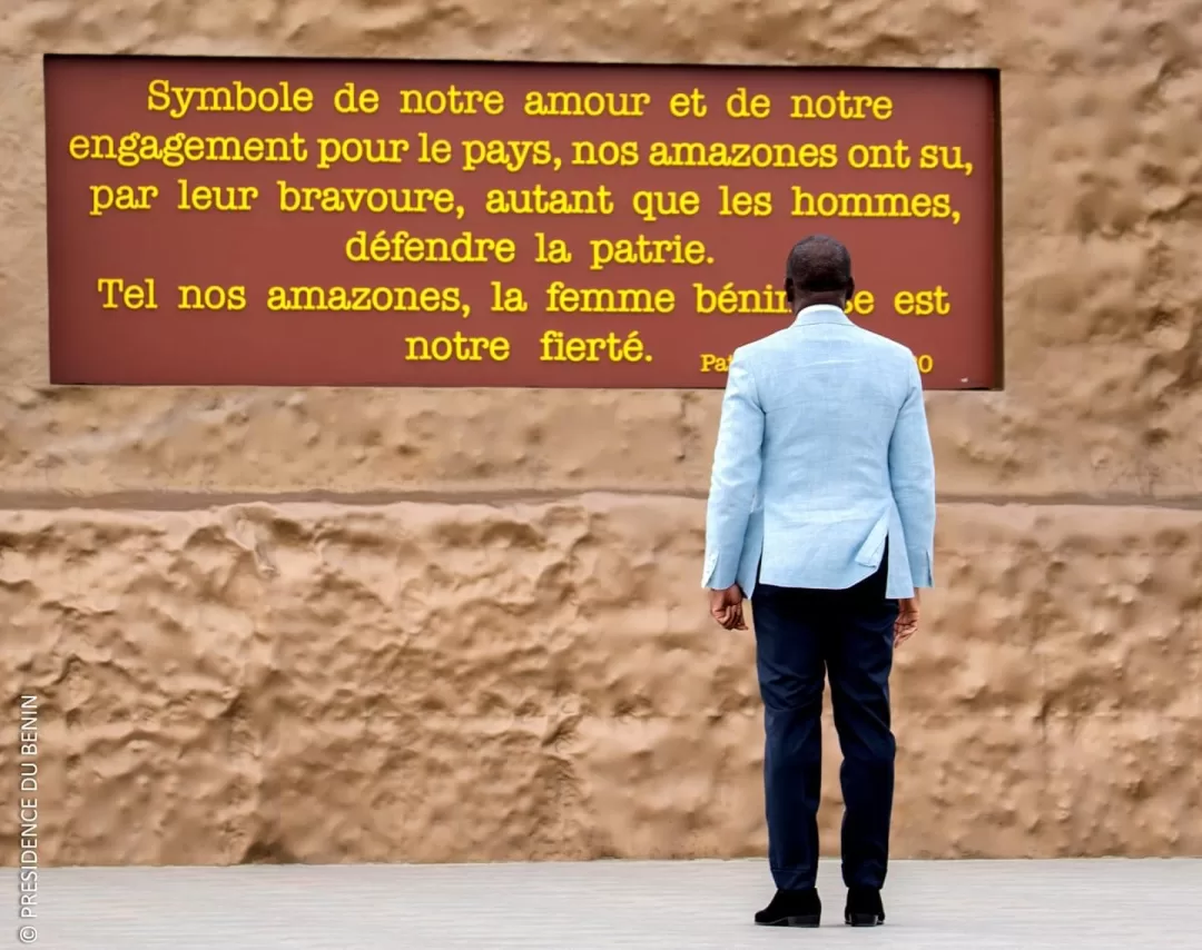 Un homme en veste claire regarde un panneau rouge avec un texte jaune contre un mur beige texturé