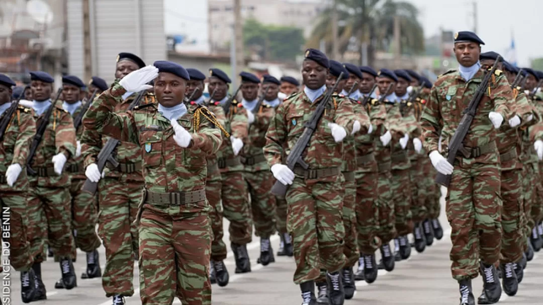 Un groupe de militaires en uniforme de camouflage défile en formation serrée dans une rue urbaine.