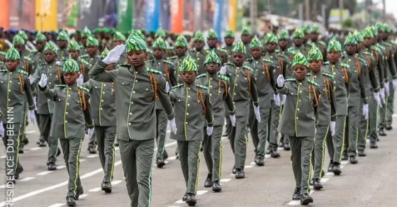 Des jeunes en uniforme militaire défilent en formation serrée dans une rue urbaine.