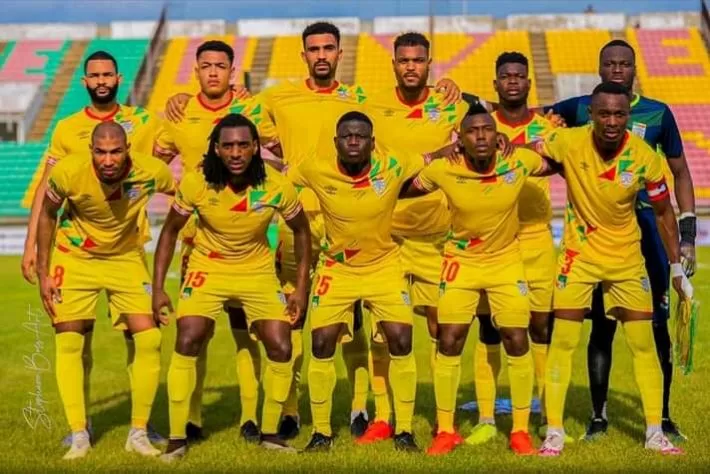 Onze joueurs en tenue jaune posant sur un terrain de football dans un stade aux gradins partiellement vides