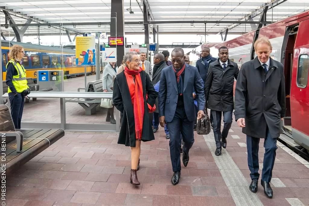 Un groupe de personnes bien habillées marche sur un quai de gare entre deux trains sous une verrière transparente