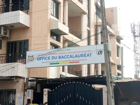 Entrée d'un bâtiment avec une bannière affichant le texte « OFFICE DU BACCALAURÉAT » suspendue au-dessus d'une porte noire.</s>