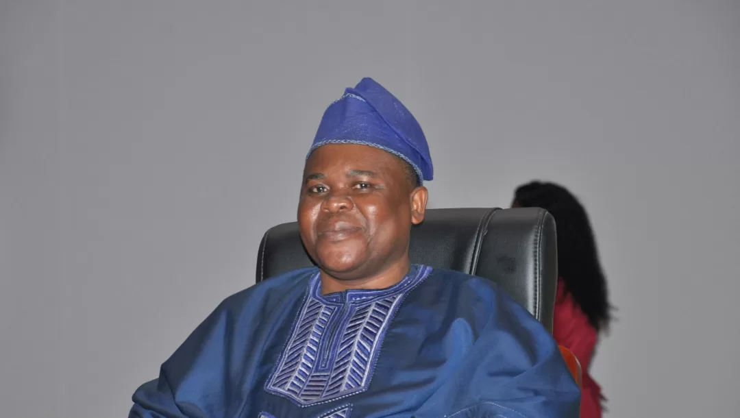 Homme souriant en tenue traditionnelle bleue assis sur une chaise devant un fond gris