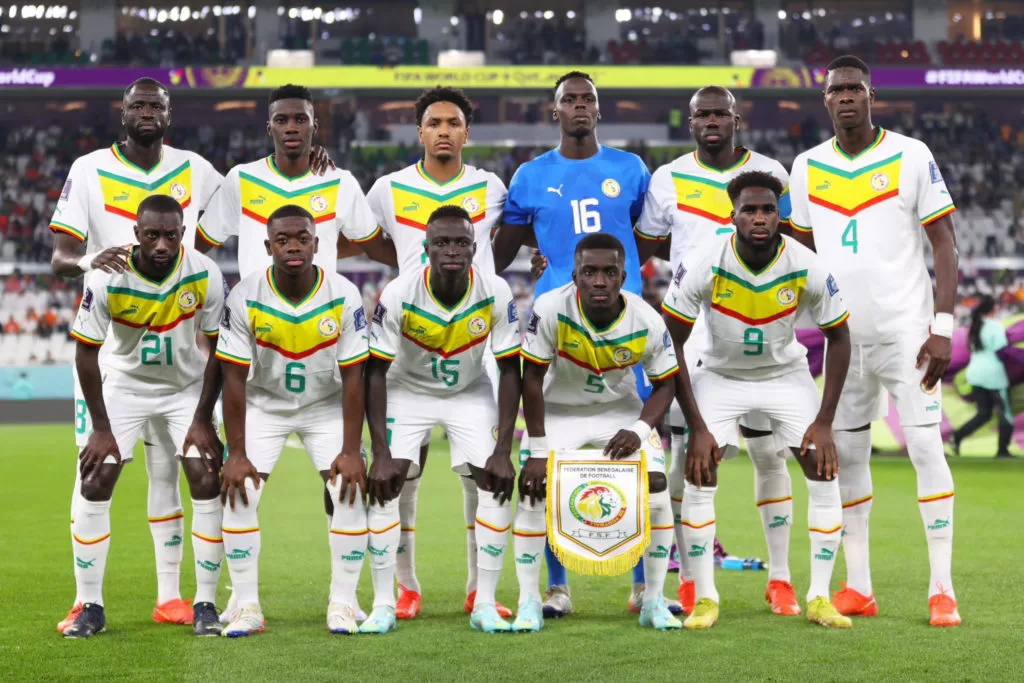 Onze joueurs de football en tenue blanche avec bandes vertes et jaunes posant sur le terrain avant un match officiel
