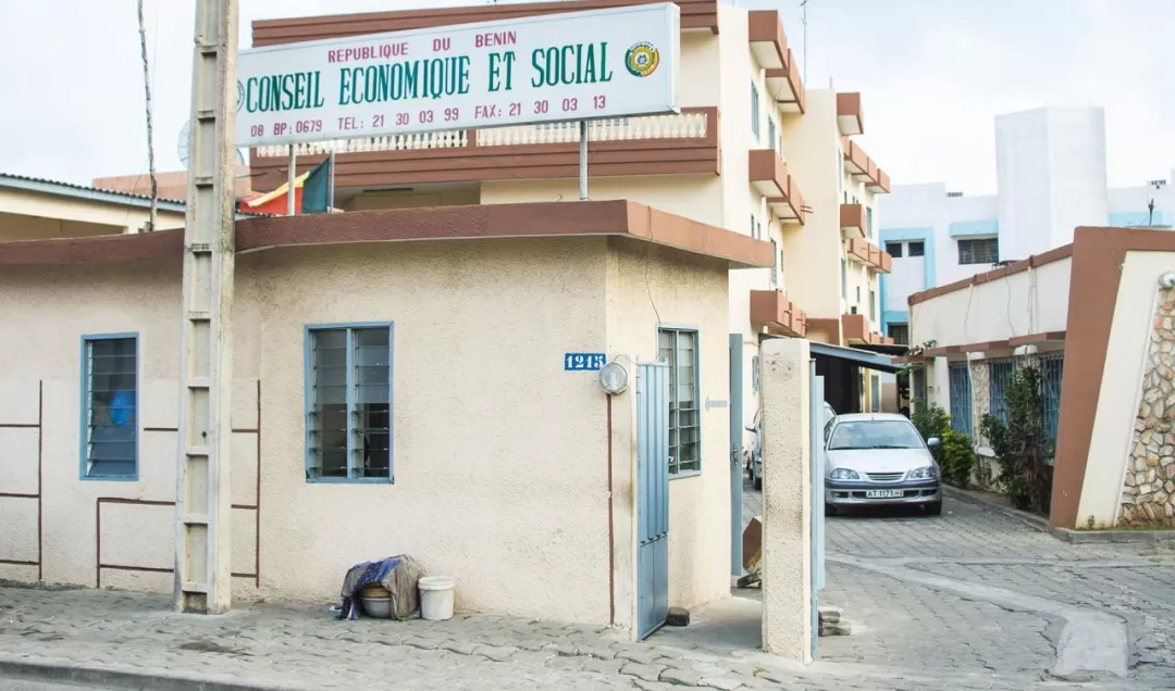 Façade d un bâtiment beige avec un panneau indiquant Conseil Économique et Social République du Bénin et une voiture garée sur une allée pavée