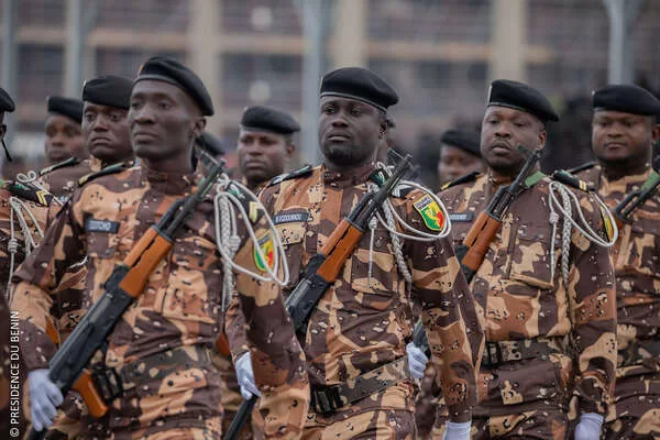 Des hommes en uniforme militaire à motifs camouflés avec bérets noirs et fusils en formation dans une rue urbaine.