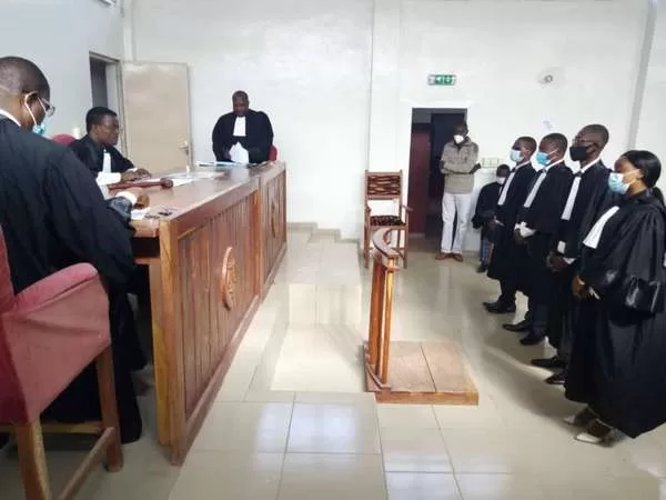 Des magistrats en robe et masques dans une salle d’audience debout face au bureau du juge assis