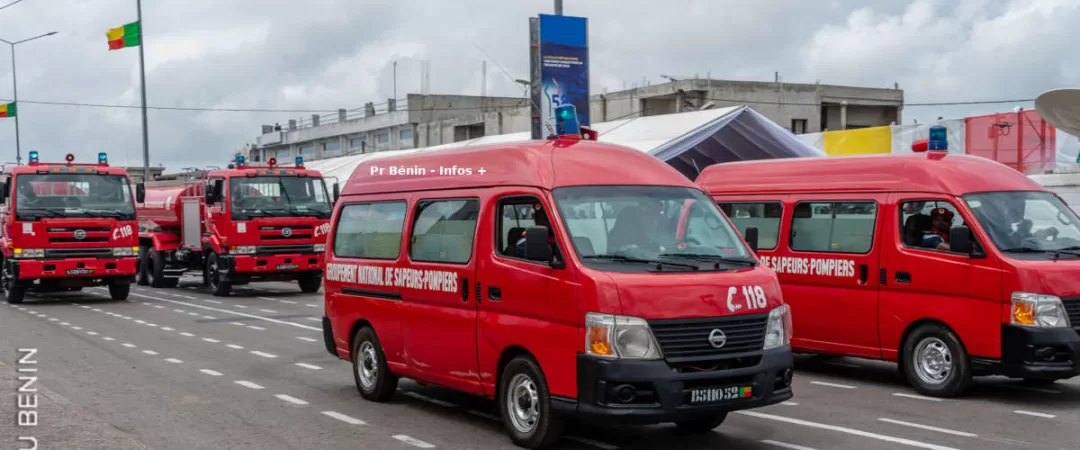 Plusieurs véhicules rouges de sapeurs-pompiers stationnés sur une large route sous un ciel nuageux