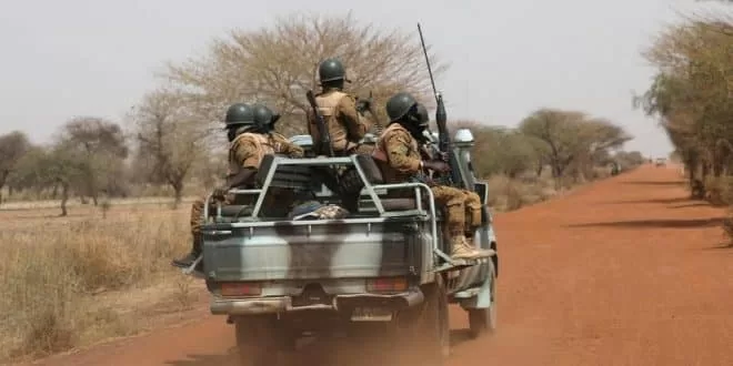 Quatre soldats en tenue et casque sont armés dans la benne d un pick-up sur une piste en terre rouge bordée d arbres secs