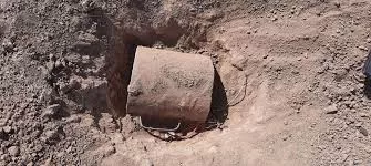 Un trou dans le sol avec un objet cylindrique en métal partiellement enterré au milieu de la terre sèche