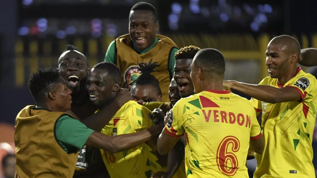 Des joueurs de football en maillots jaunes célèbrent ensemble sur le terrain lors d’un match de nuit