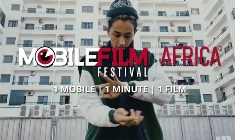 Jeune homme debout en extérieur devant des immeubles, effectuant un geste avec ses mains, texte Mobile Film Festival Africa en surimpression