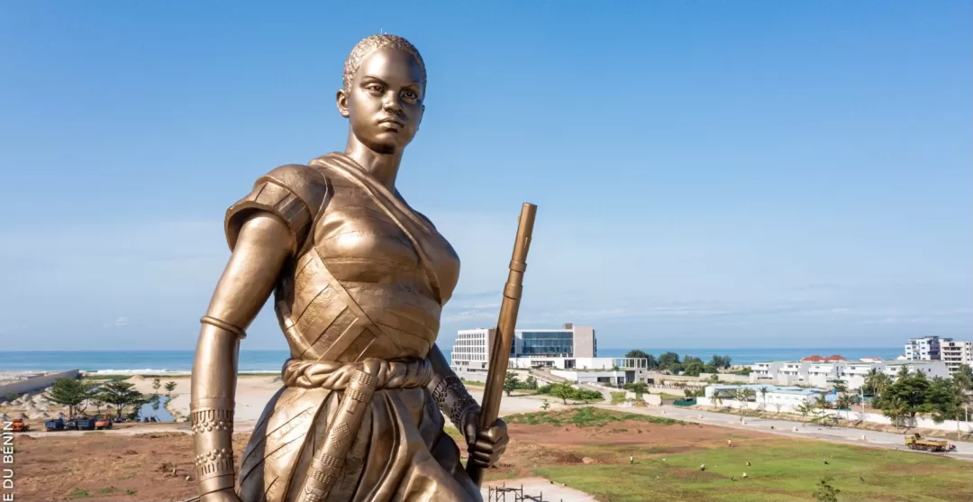 Statue en bronze d'une femme tenant un fusil, avec un paysage urbain et la mer en arrière-plan