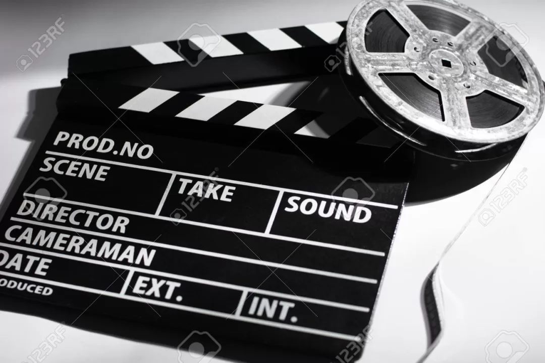 Clap de cinéma noir et blanc et une bobine de film argentique posés sur une surface blanche