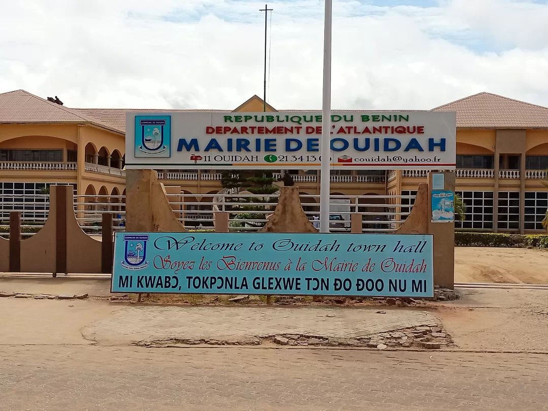 Façade d un bâtiment municipal avec plusieurs panneaux indiquant la mairie de Ouidah et un message de bienvenue multilingue