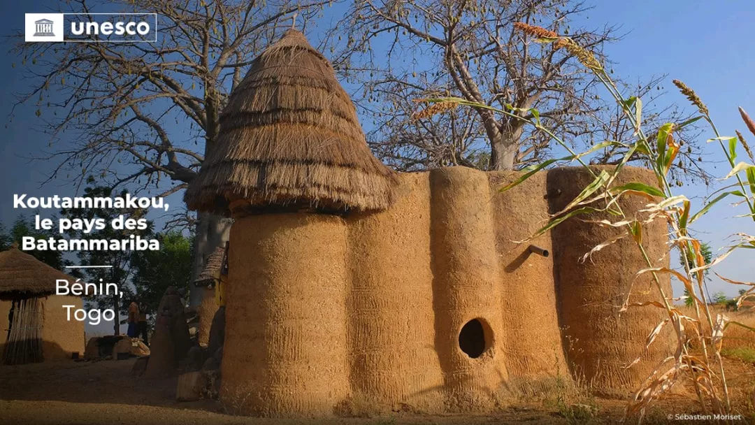 Habitat traditionnel en terre avec toiture en chaume sous un ciel bleu et arbres autour en pleine journée