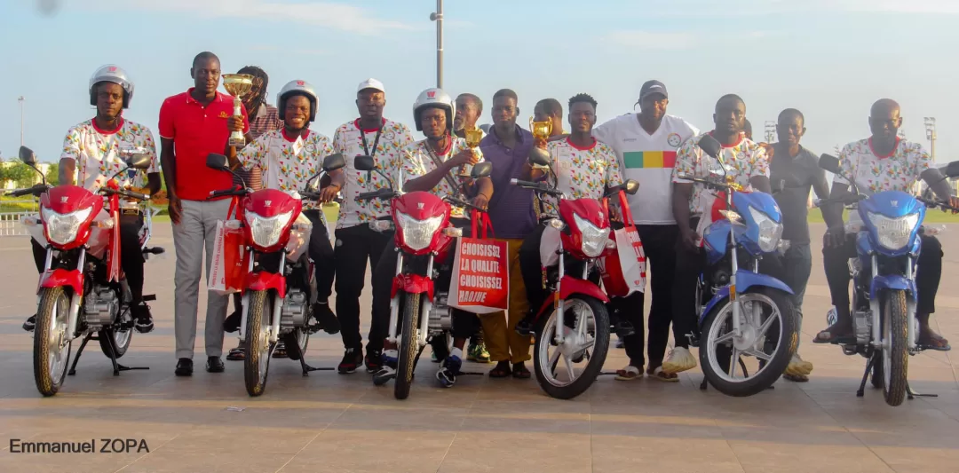 Dix hommes debout alignés avec des motos rouges et bleues, certains tenant des trophées et un panneau rouge.
