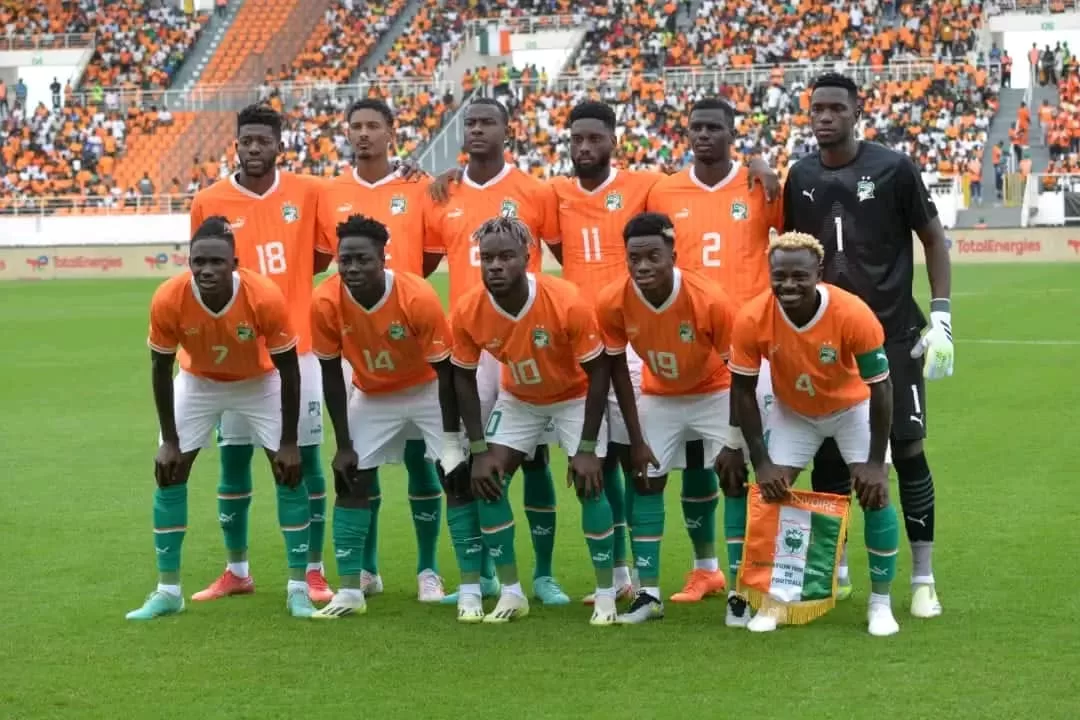 Onze joueurs de football en tenue orange et blanche posent sur un terrain devant des tribunes partiellement remplies