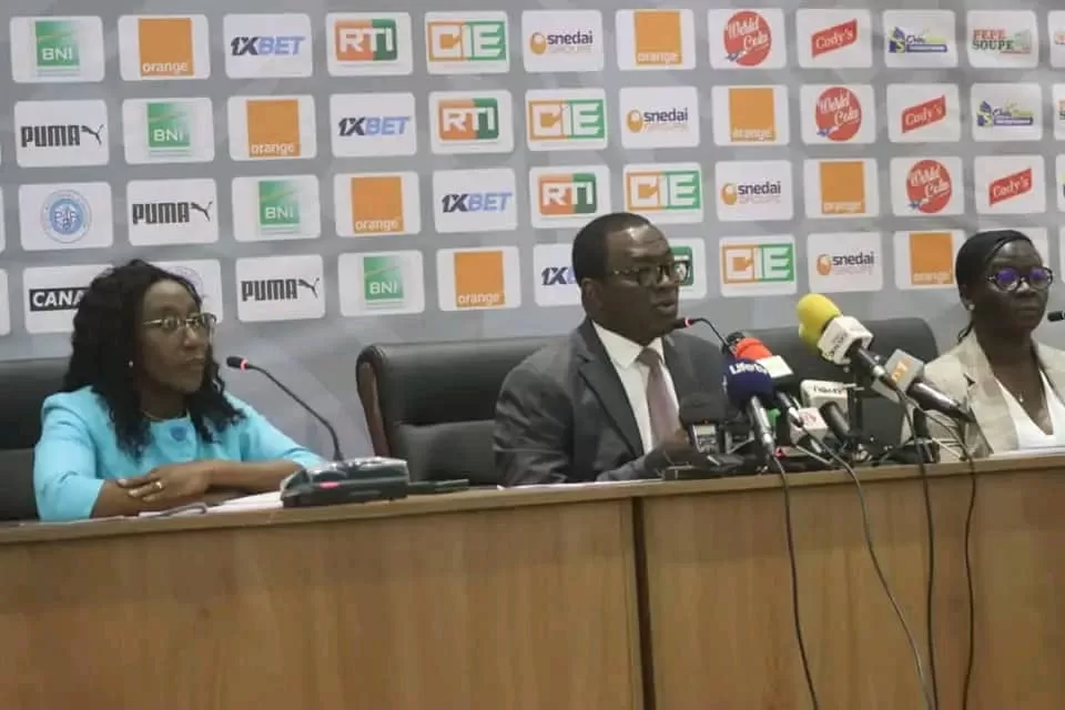 Trois personnes assises derrière un pupitre lors d’une conférence de presse avec plusieurs micros visibles