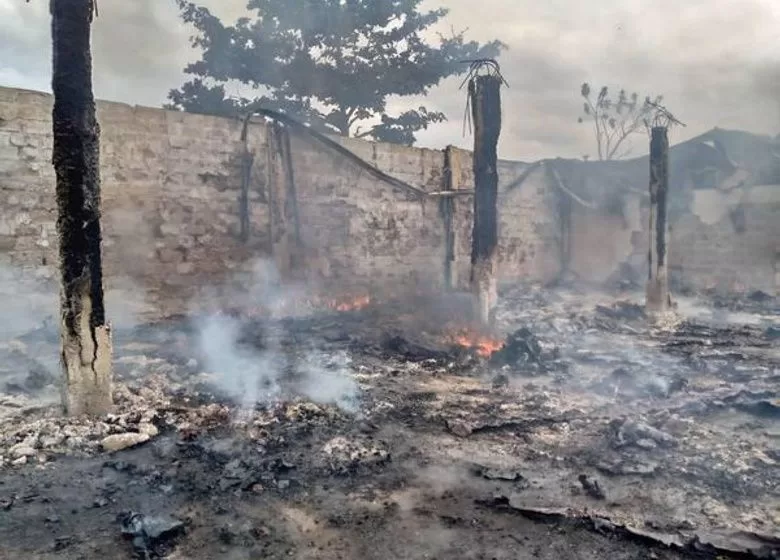 Terrain ravagé par un incendie avec des débris brûlés encore fumants et des piliers carbonisés d’une structure détruite