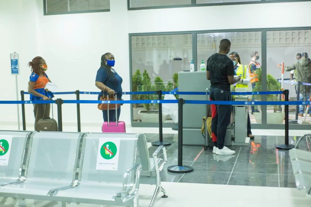 Personnes masquées en file d'attente dans un espace d'attente avec des chaises et un contrôle sanitaire en arrière-plan