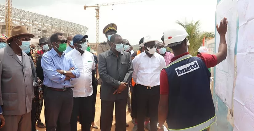 Un groupe d’hommes en tenue formelle et casques observe un plan affiché sur un chantier avec une grue en arrière-plan