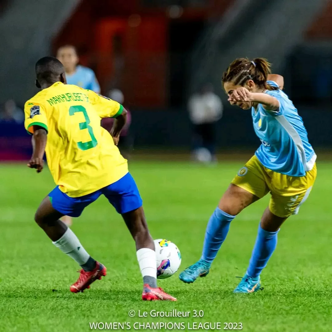 Deux joueuses de football en duel pour le contrôle du ballon sur un terrain vert lors d’un match nocturne
